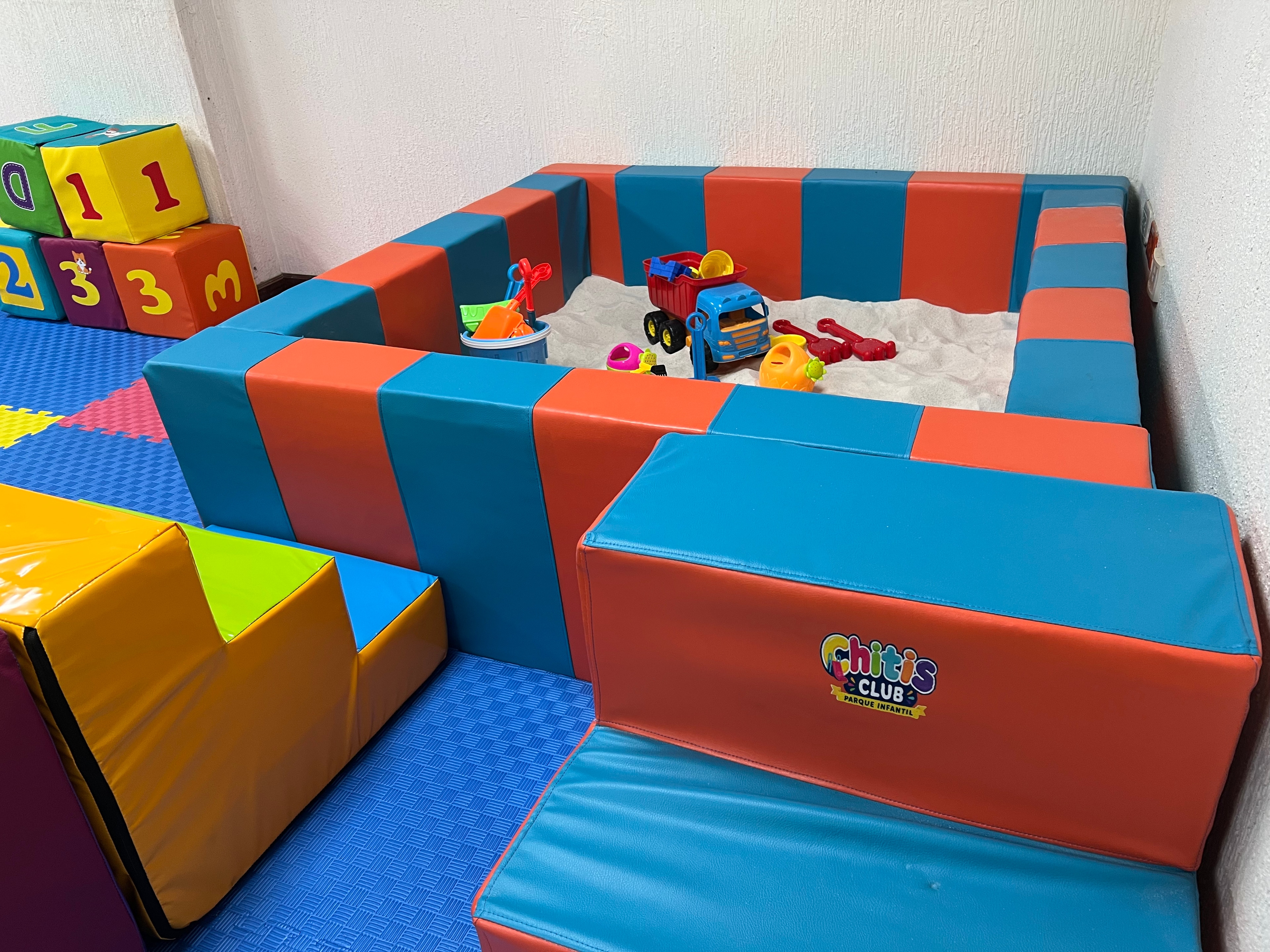 Zona de bebés de Chitis Club con arenero y elementos de juego acolchados.